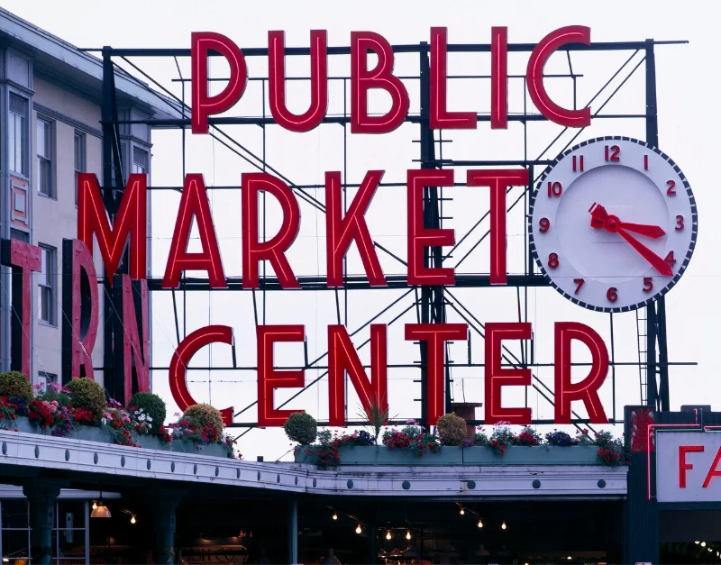 Pike Place Market’s red Public Market Center sign and clock above flower baskets
